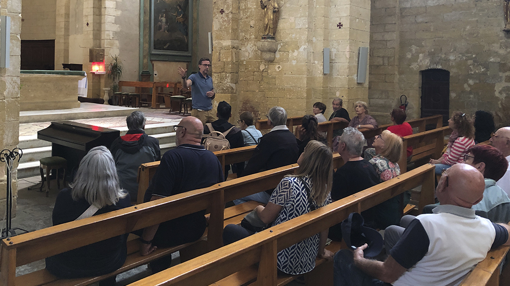 Un groupe de personne assises dans une église écoutent les explication d'un guide touristique