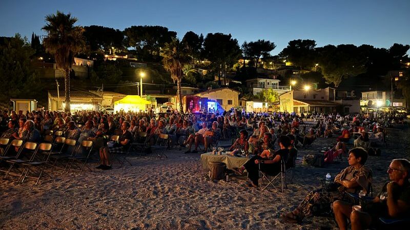 Concert de jazz de nuit sur la plage sable palmier foule assise et debout 