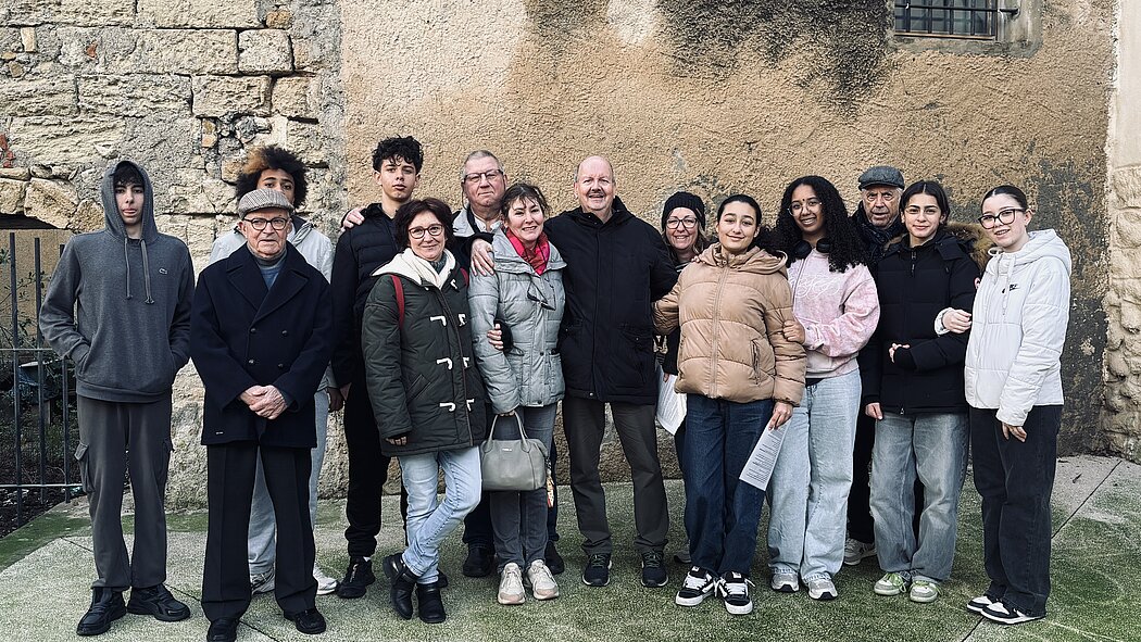     Requête réussie  Gemini said  Cette photo montre un groupe de treize personnes posant ensemble en extérieur, devant un mur de pierre ancienne et de crépi. L'ambiance semble être celle d'une réunion familiale ou amicale par un temps frais.  Voici une description plus détaillée de l'image : Le Groupe  Le groupe est composé d'hommes et de femmes de différents âges. Ils sont disposés sur deux rangs informels :      Au centre : Un homme avec un manteau noir semble être le point central, entouré de plusieurs femmes qui sourient.      À gauche : On remarque un homme plus âgé portant une casquette et un caban bleu marine, ainsi qu'un jeune homme en sweat à capuche gris.      À droite : Plusieurs jeunes femmes et un homme plus âgé avec une casquette plate complètent le groupe.      Interactions : Plusieurs personnes se tiennent par l'épaule ou le bras, ce qui suggère une grande proximité et une atmosphère chaleureuse.