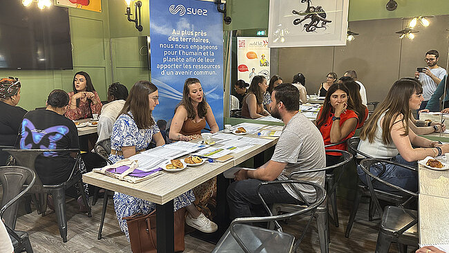 Des personnes, femmes et hommes, assis autour de plusieurs tables