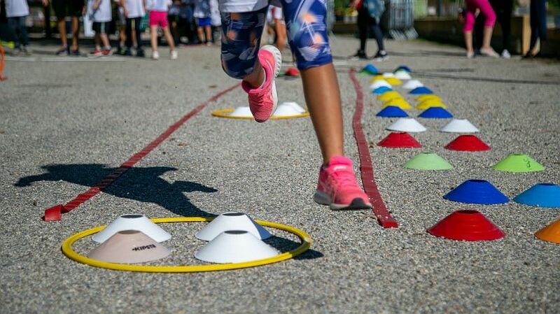 Une activité en plein air où un enfant court parmi des cônes colorés disposés sur le sol, entouré d'autres enfants.