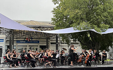 groupe de musique classique sur scène à l'extérieur avec voiles d'ombrage et arbre 