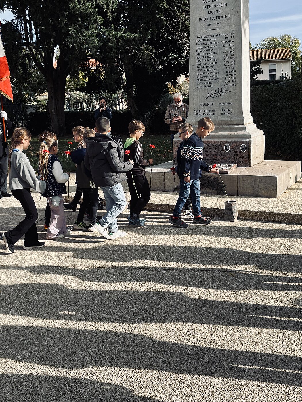 Des enfants déposent des oeillets rouge devant le monument aux morts d'Entressen