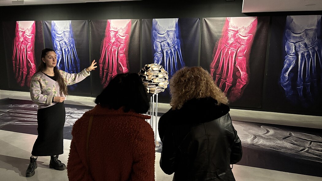 deux femment ecoute l'explication d'un tableau fait par une autre femme