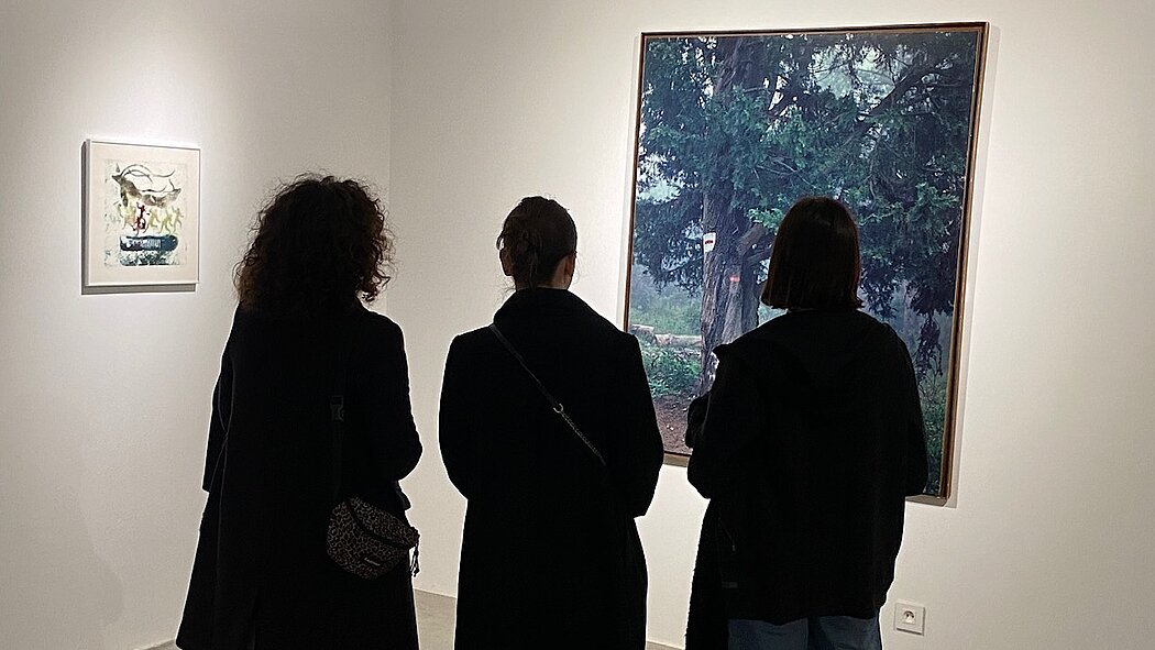 Trois femmes regardent un grand tableau qui semble être une photographie d'un arbre magestueeux