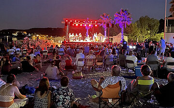 Concert avec podium sur plage la nuit foule assise sur le sable
