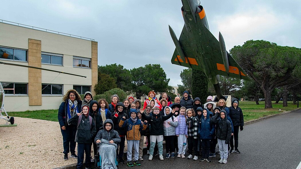 Cette photo montre un grand groupe composé d'enfants et de quelques adultes. Ils posent devant des aéronefs (un hélicoptère et un avion de chasse) lors de la visite de la BA125