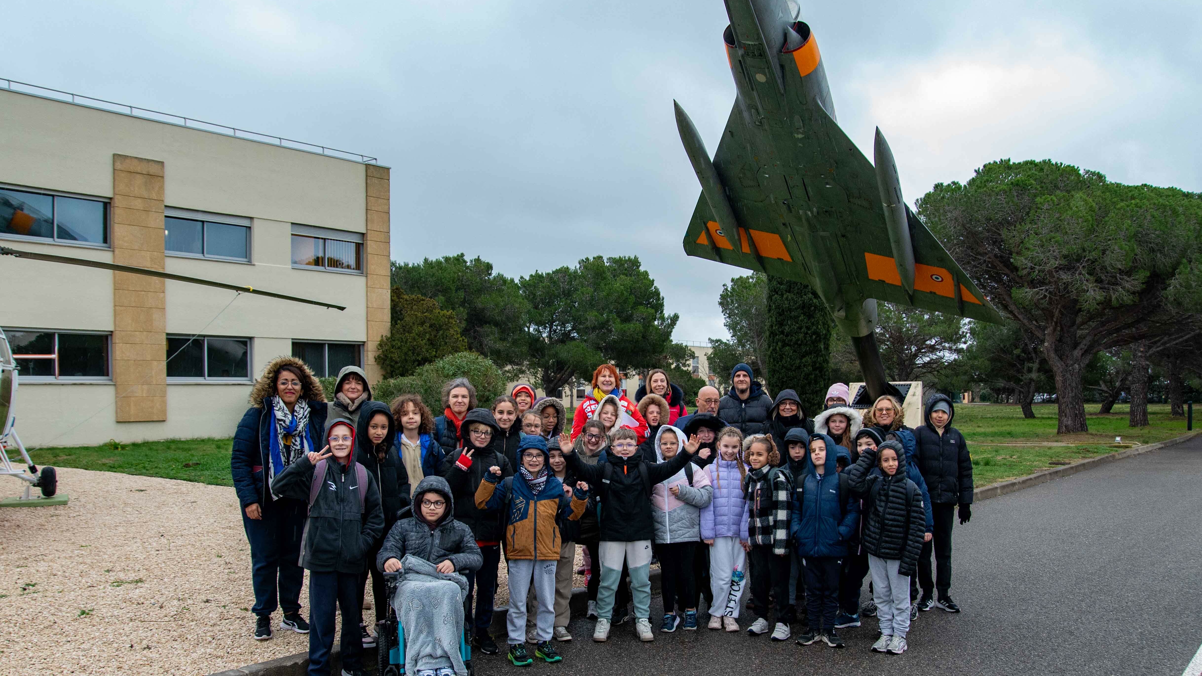 Cette photo montre un grand groupe composé d'enfants et de quelques adultes. Ils posent devant des aéronefs (un hélicoptère et un avion de chasse) lors de la visite de la BA125