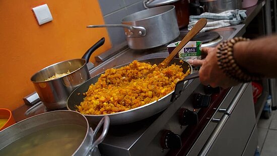 La première image montre une cuisinière avec plusieurs casseroles et poêles. Au premier plan, une grande poêle contient un mélange de légumes cuisinés de couleur orangée. Une main tenant une spatule en bois mélange la préparation. À l’arrière, on distingue d’autres casseroles en métal et un petit carton vert et blanc de crème de coco posé près de la poêle.