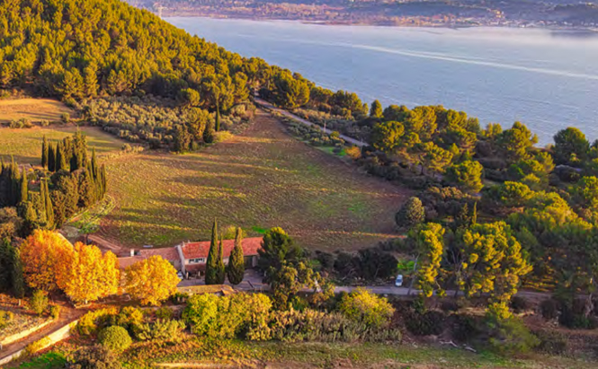 Vue aérienne du domaine de conclué : mas/grande maison au milieu de champs  arbre verdure et étang au loin 