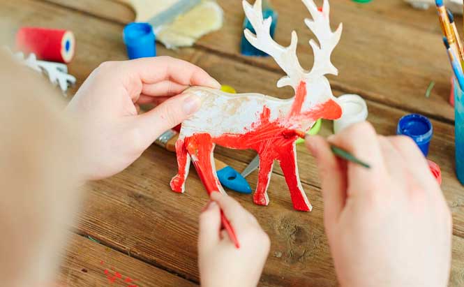 ChatGPT a dit :  L'image montre deux mains, celles d'un enfant et d'un adulte, peinturant ensemble une figurine en forme de renne. Le renne est en bois et il est partiellement peint en rouge. Des pinceaux, des pots de peinture et des rouleaux sont visibles autour de la figurine sur la table en bois. L'arrière-plan montre des éléments de peinture comme des bouchons de plastique et d'autres outils créatifs. La scène semble se dérouler dans un environnement créatif, avec des couleurs vives et des matériaux d'art disposés autour.