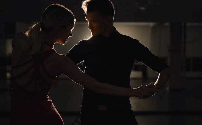 ChatGPT a dit :  L'image montre deux personnes dans une posture de danse, probablement un couple en train de danser. L'homme et la femme sont vus de profil, avec des silhouettes distinctes mais en contre-jour. La lumière provient principalement de l'arrière, créant un effet de halo autour d'eux. L'homme porte une chemise noire et la femme un vêtement rouge, probablement une robe de danse. Ils tiennent leurs mains l'un l'autre dans une position de danse élégante et rapprochée. Le décor en arrière-plan est sombre, avec seulement quelques ombres et contours visibles.